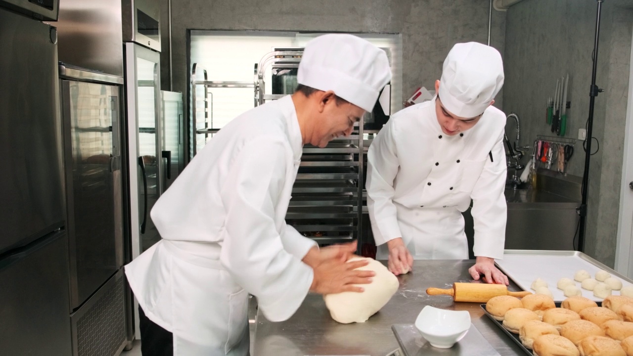 身着制服的亚洲男厨师正准备在一个不锈钢厨房里烤面包。视频下载