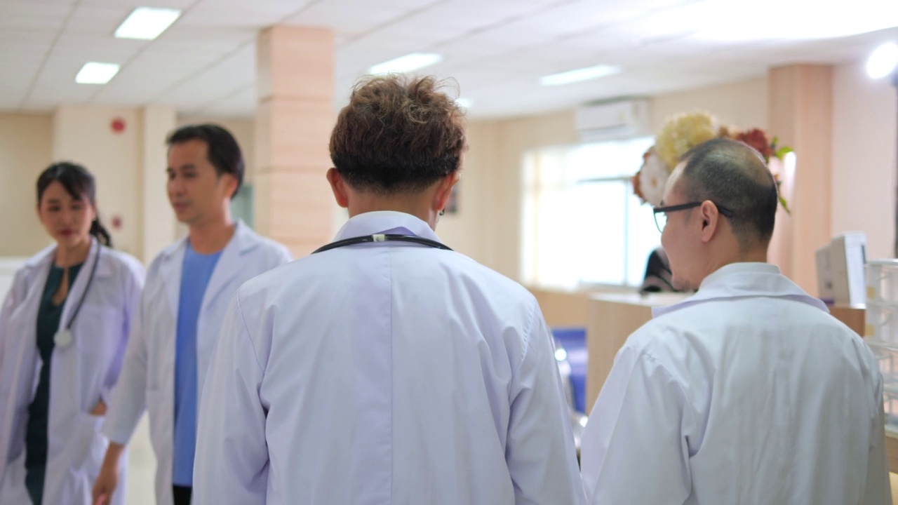后视图两个严肃的亚洲医生团队走过医院的走廊，他们交谈和讨论病人的诊断数据持有数字平板电脑技术。视频下载