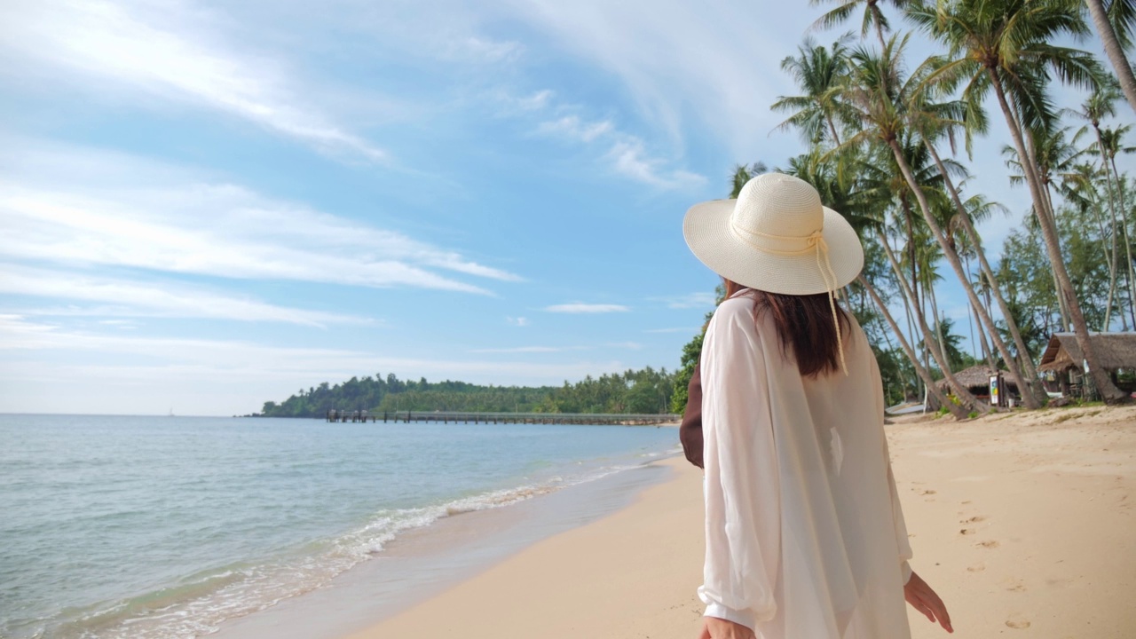 女人站在沙滩上举手的背影。假期，假期，放松的夏季生活方式。视频素材