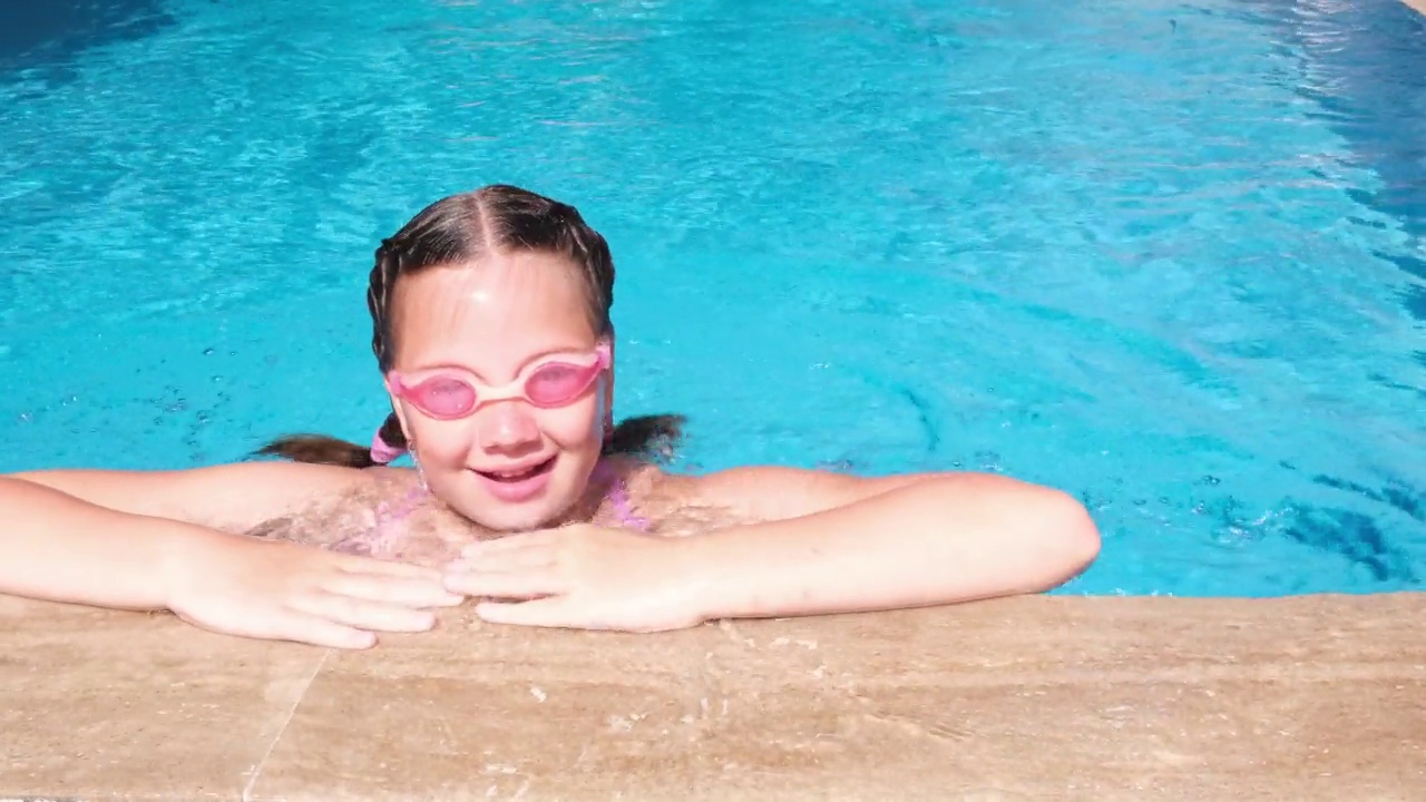 可爱的女孩在游泳池里的粉红色水杯。女孩浮出水面视频下载