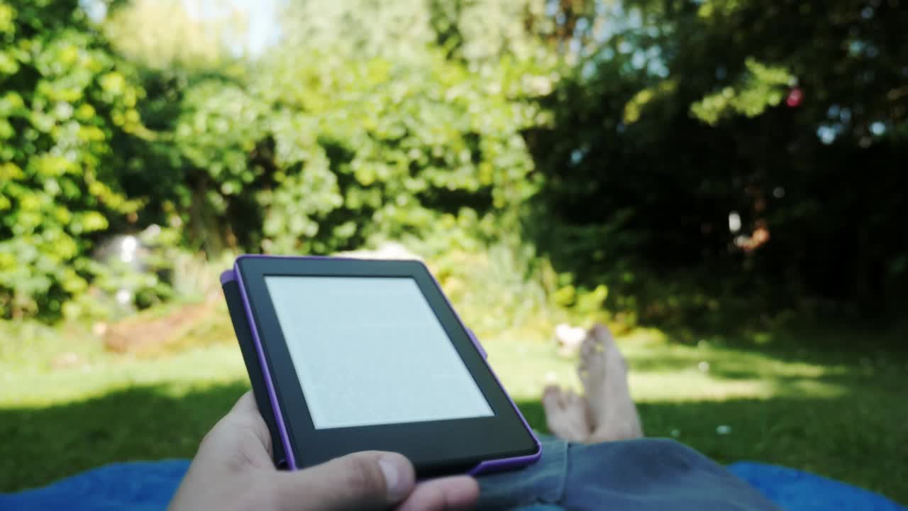 快乐的男女学生阅读电子书，躺在花园的椅子上。电子书让人放松。生活方式，休闲和放松在家里视频素材