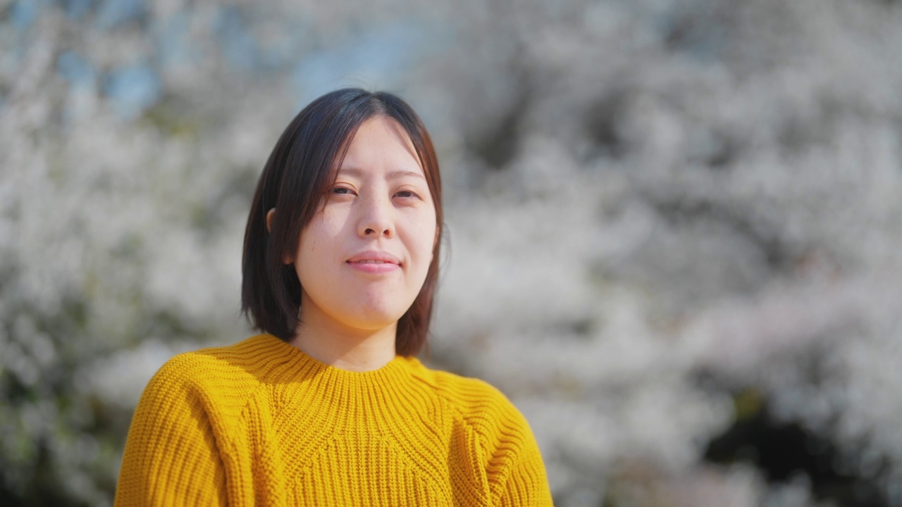 年轻女子在樱花樱花树前野餐的肖像视频下载