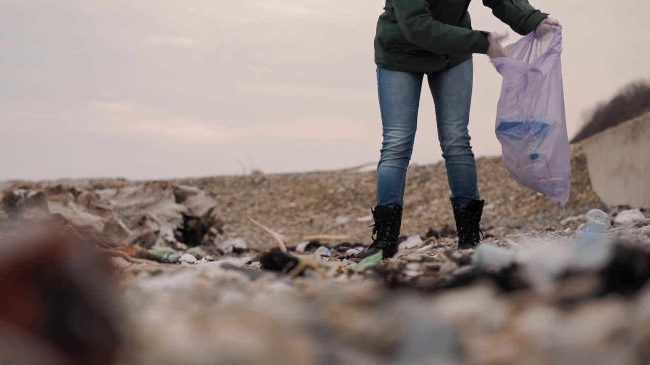 地球日。一名女性志愿者在海滩上收集垃圾，并将其放入垃圾袋。环境污染和环境保护的概念视频素材