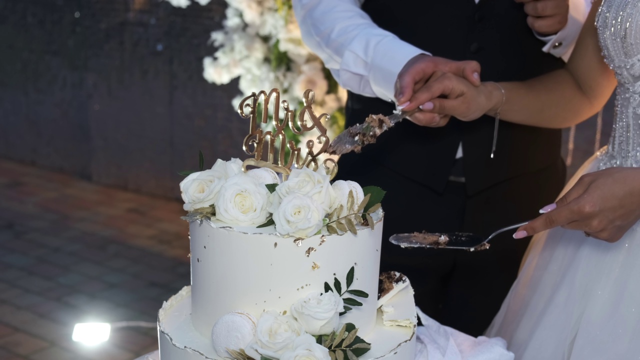 美丽的婚礼蛋糕。新娘和新郎切了一块蛋糕。手的特写镜头。婚礼仪式。视频下载