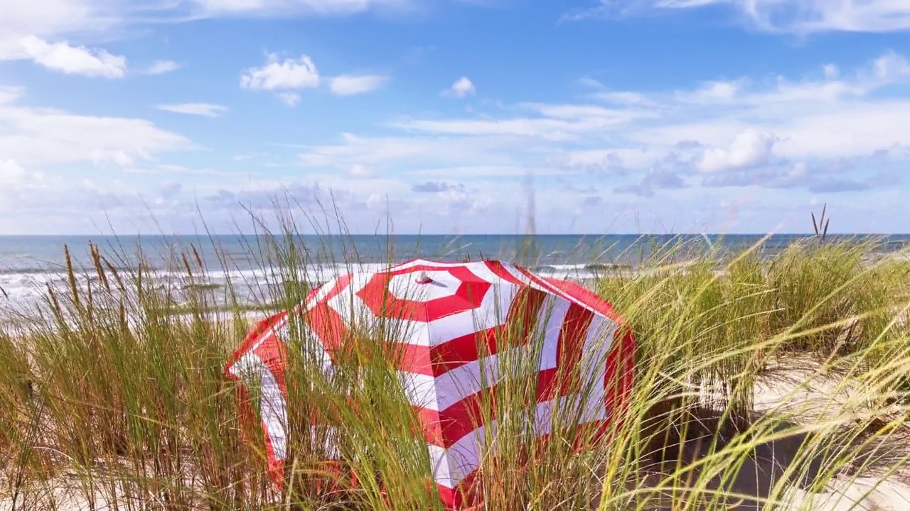 红白条纹阳伞在沙丘对着大海和天空视频素材