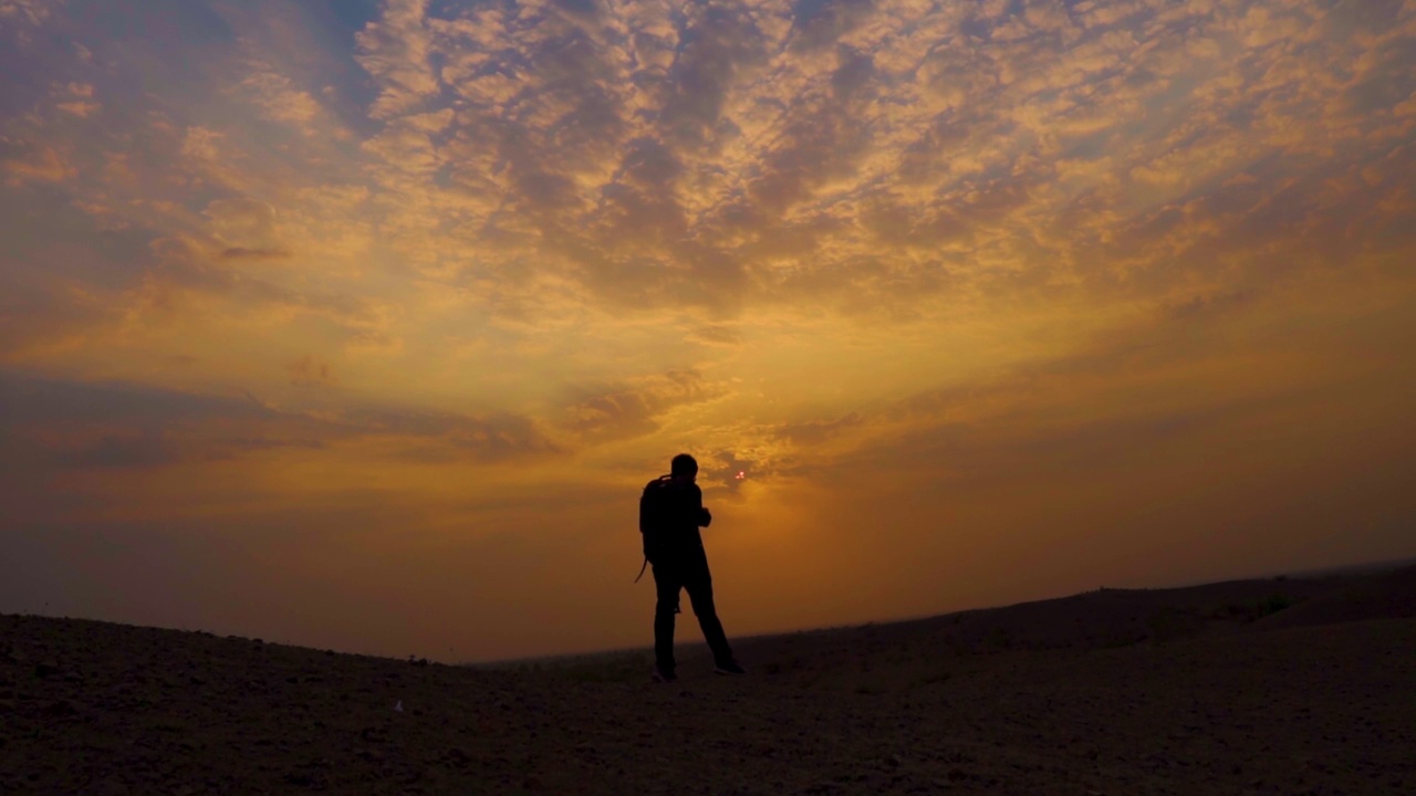 一个印度徒步旅行者在日落前的山顶上行走的剪影。自然背景。日落时分，一个人走在橙色的云彩和太阳前面。视频素材