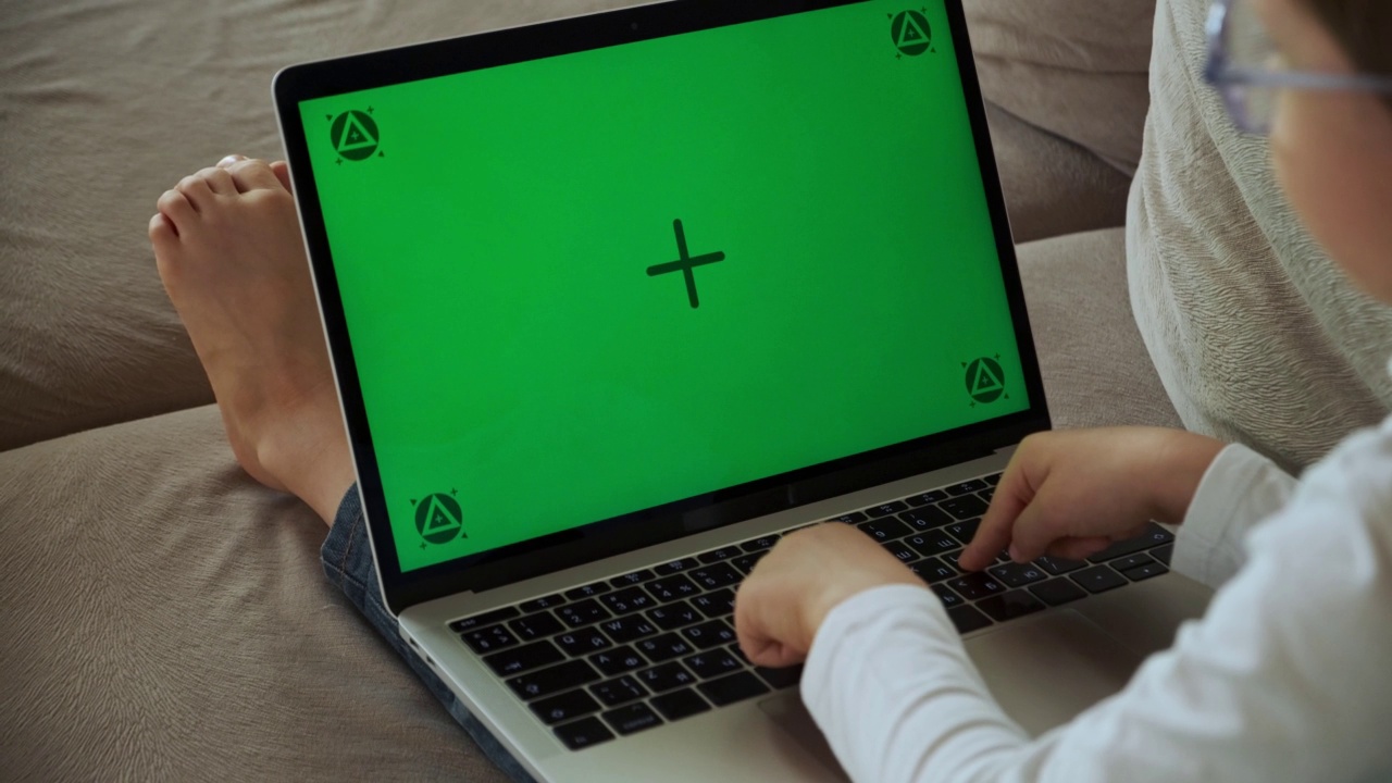 孩子用笔记本电脑的绿屏色度键，打字和电子学习，躺在家里的沙发上视频下载