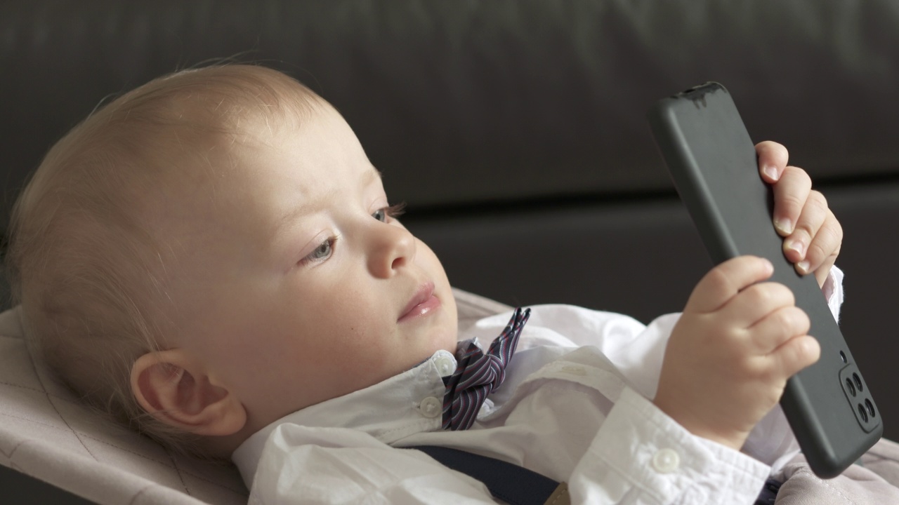 孩子玩手机玩得很开心，一岁的小男孩拿着手机，可爱的幼儿玩智能手机的照片。儿童和移动技术。视频素材