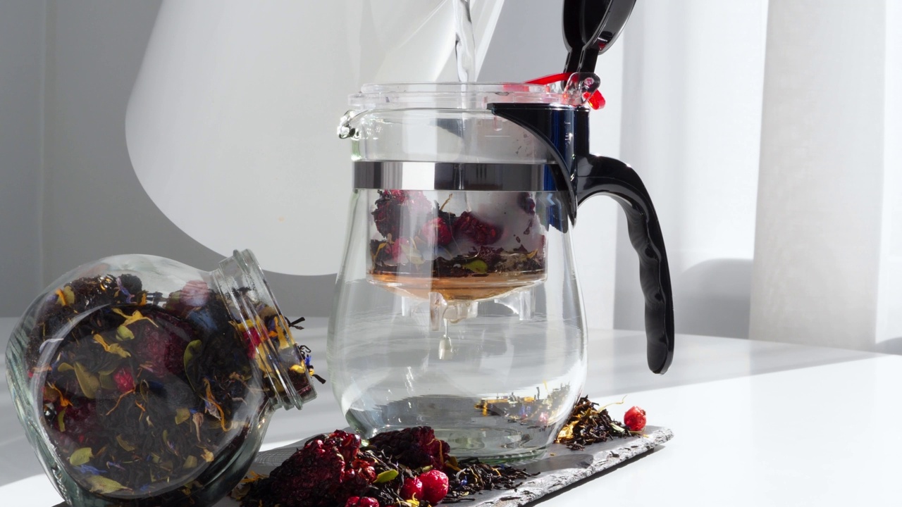 将热水、沸水倒入透明的玻璃茶壶中。泡茶收集茶叶，黑莓，蓝莓，蔓越莓，香草。家茶。泡茶的过程红茶与自然视频素材