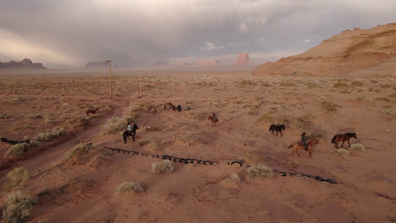 无人机纳瓦霍青少年在亚利桑那州的纪念碑谷部落公园骑马，黄昏时分，在戏剧性的云景下视频下载