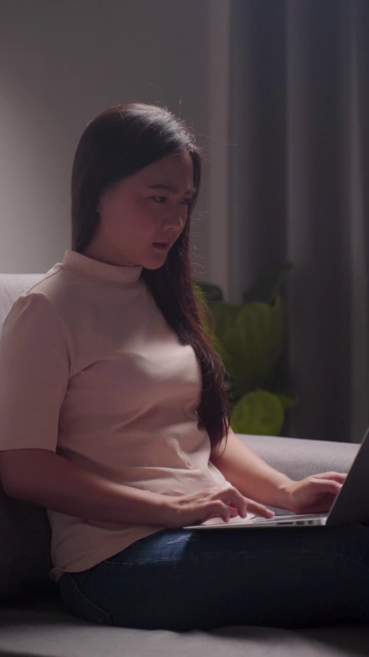 亚洲女性在使用笔记本电脑工作时头痛，摸着头感觉过度劳累。垂直视频。视频下载