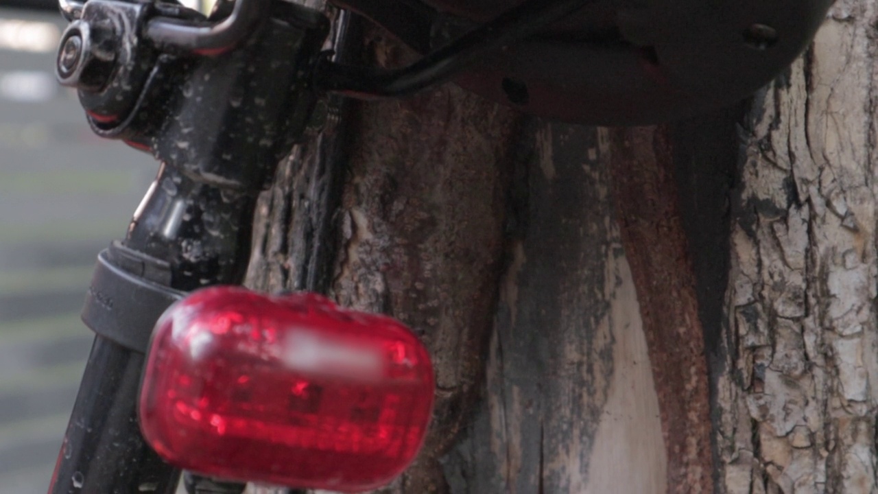 自行车红色LED闪烁尾灯。一辆停在树旁闪着红灯的自行车后面的镜头。自行车闪光器在行动视频素材