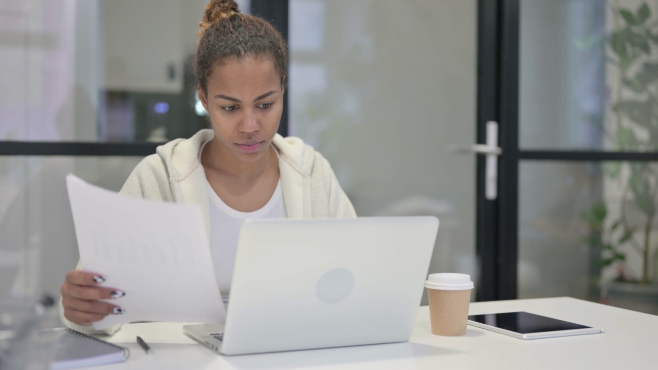 一名非洲妇女一边用笔记本电脑阅读文件，一边庆祝成功视频素材