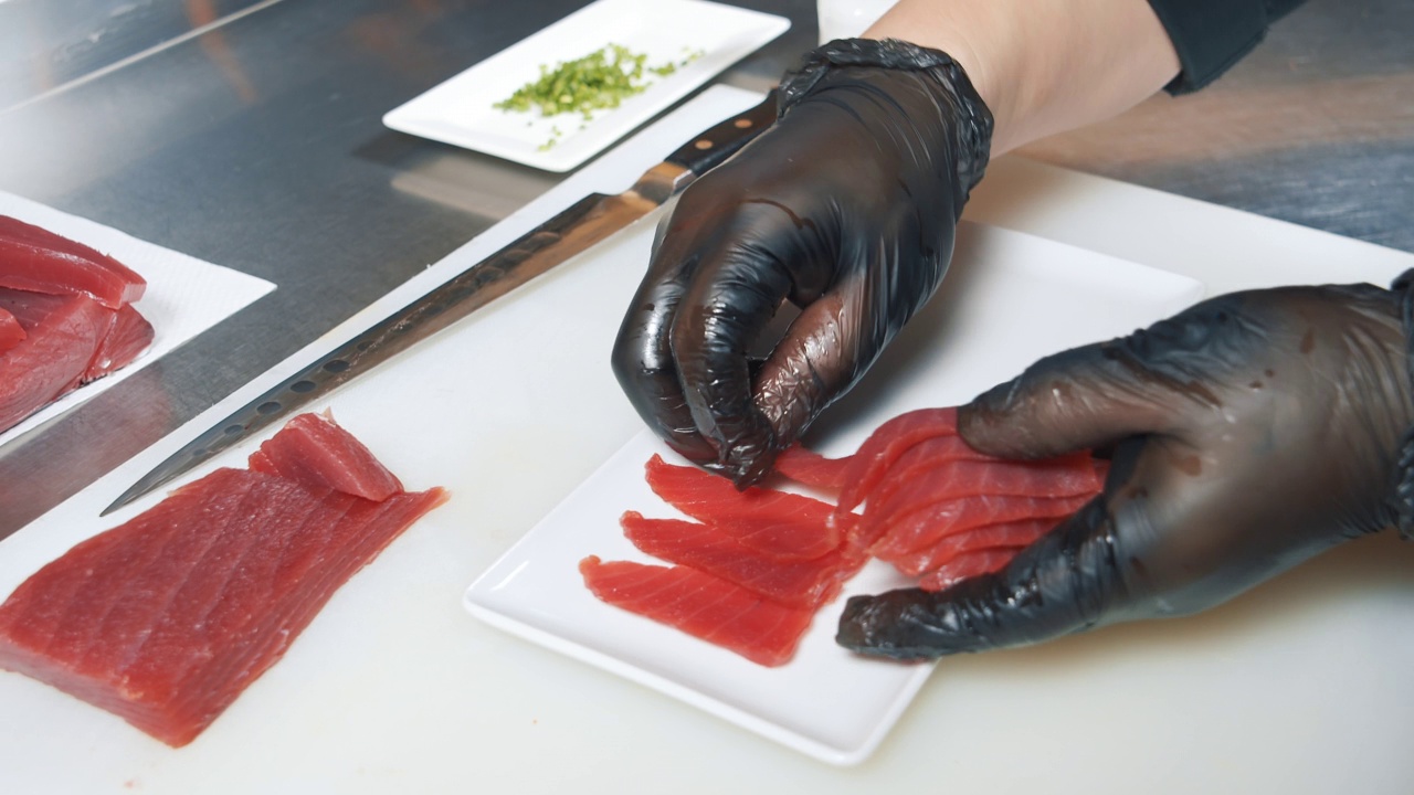 一个戴着手套的厨师的男性手的特写镜头切片新鲜的金枪鱼。传统的日本料理。视频素材