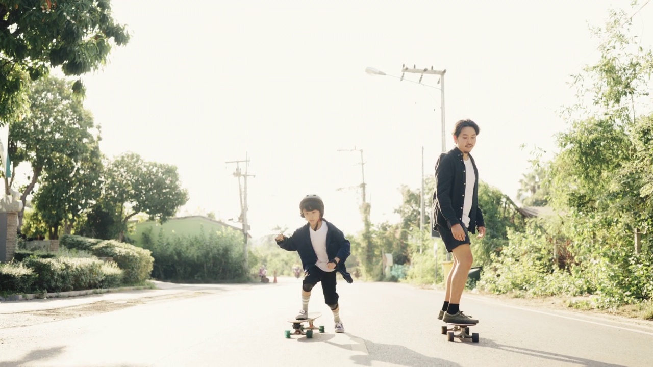 亚洲父亲和儿子滑板练习在公园。视频下载