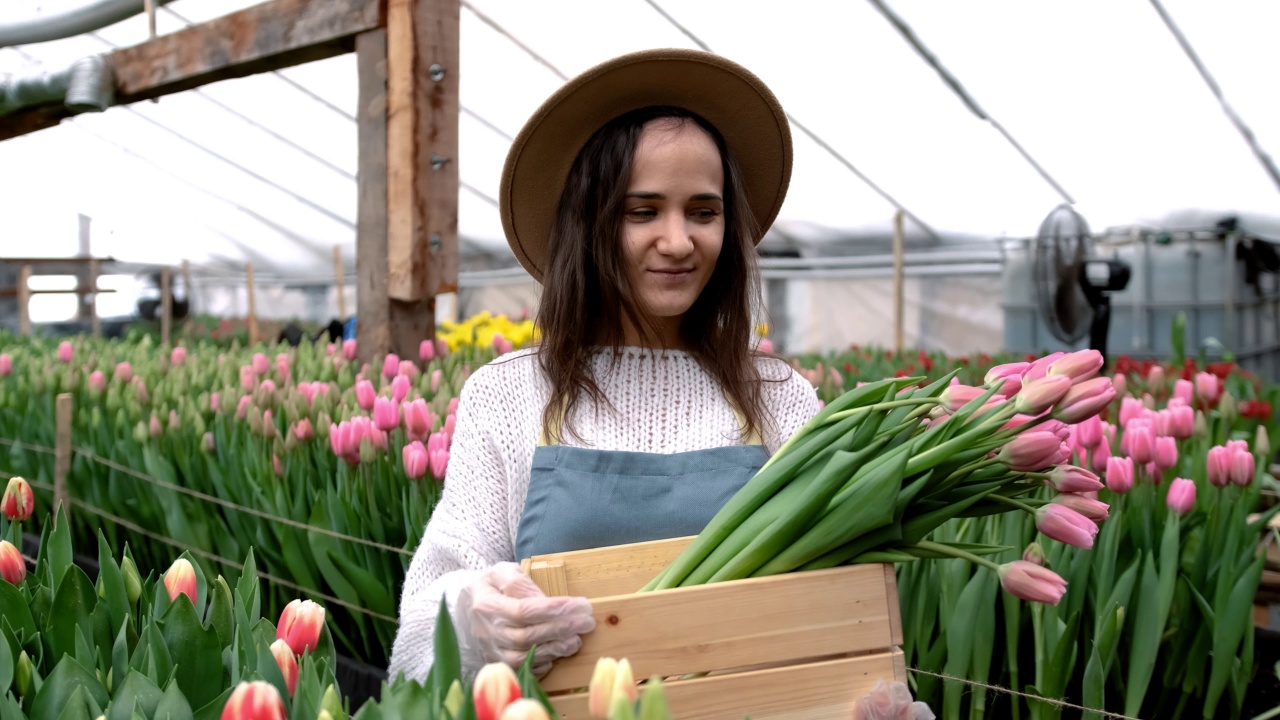 一个年轻的农民女孩戴着帽子，手里拿着一个木盒，里面放着郁金香花束。一位白人妇女正在展示一个小型家庭花卉企业的产品视频素材