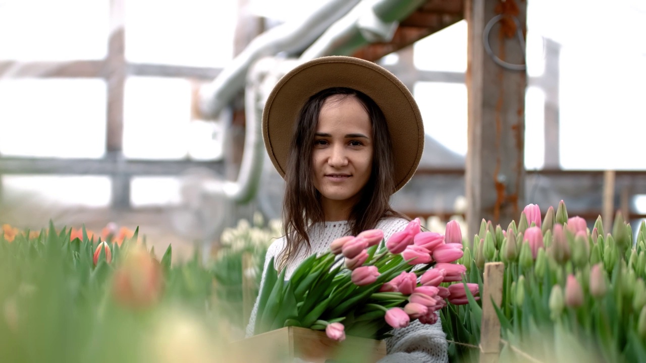 漂亮的年轻女花匠或农艺师，穿着工作服，帽子和围裙，拿着一盒羽扇豆视频素材