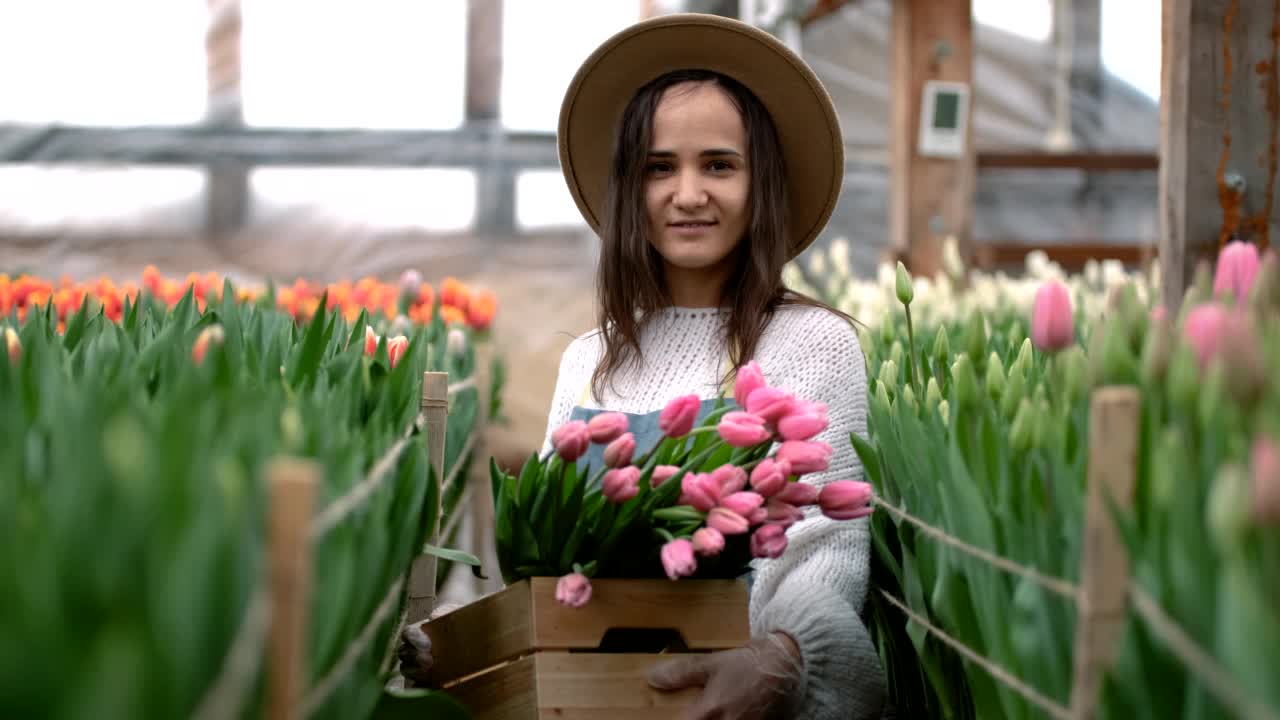 一个戴着帽子的年轻女园丁的肖像，她手里拿着一个木盒，里面放着郁金香花束，生意很好视频素材