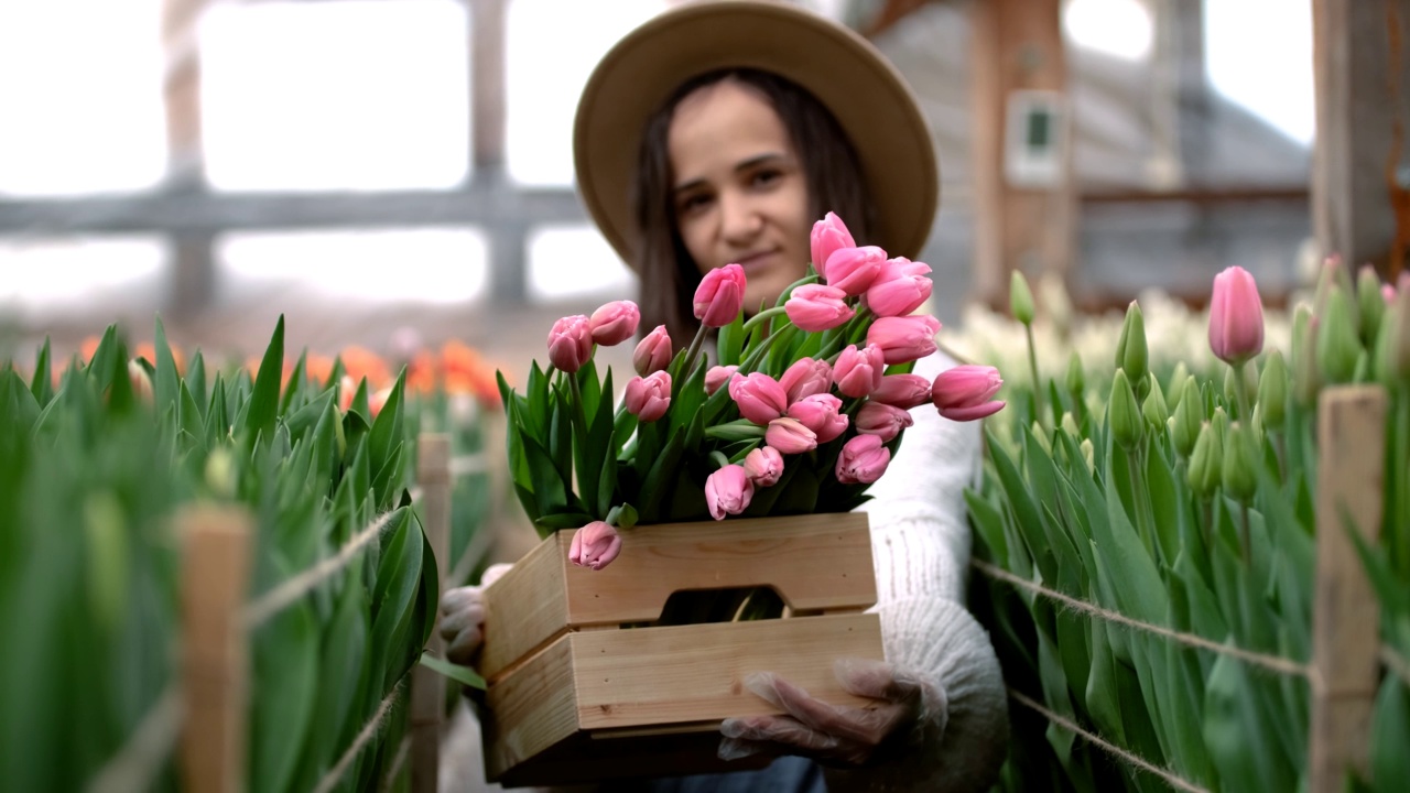 年轻的园丁戴着帽子，拿着一个装着郁金香花束的木箱视频素材