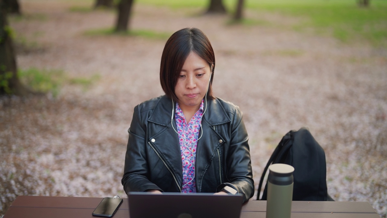 年轻女子在公园里用笔记本电脑视频下载