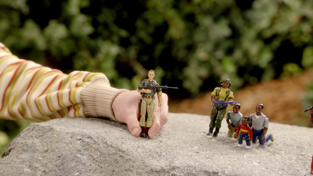 放大的动作人物玩具持有的枪。可能是士兵。孩子的手可见。可能是在后院玩。其他可以在石头上看到的动作玩偶。视频下载