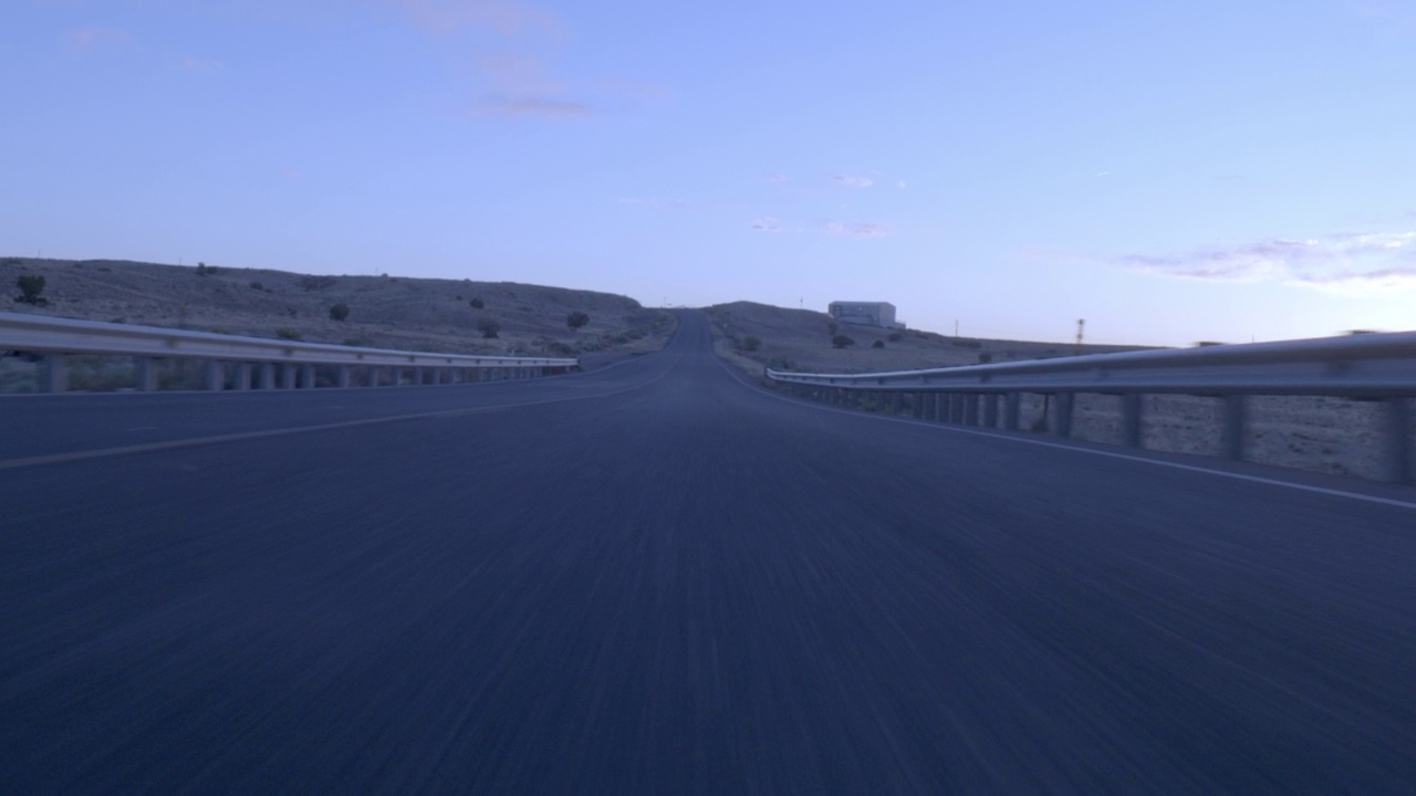 在日出或黎明时分，在沙漠公路或高速公路上行驶的汽车可直接向前加工板材。可见部分干草和灌木。视频素材