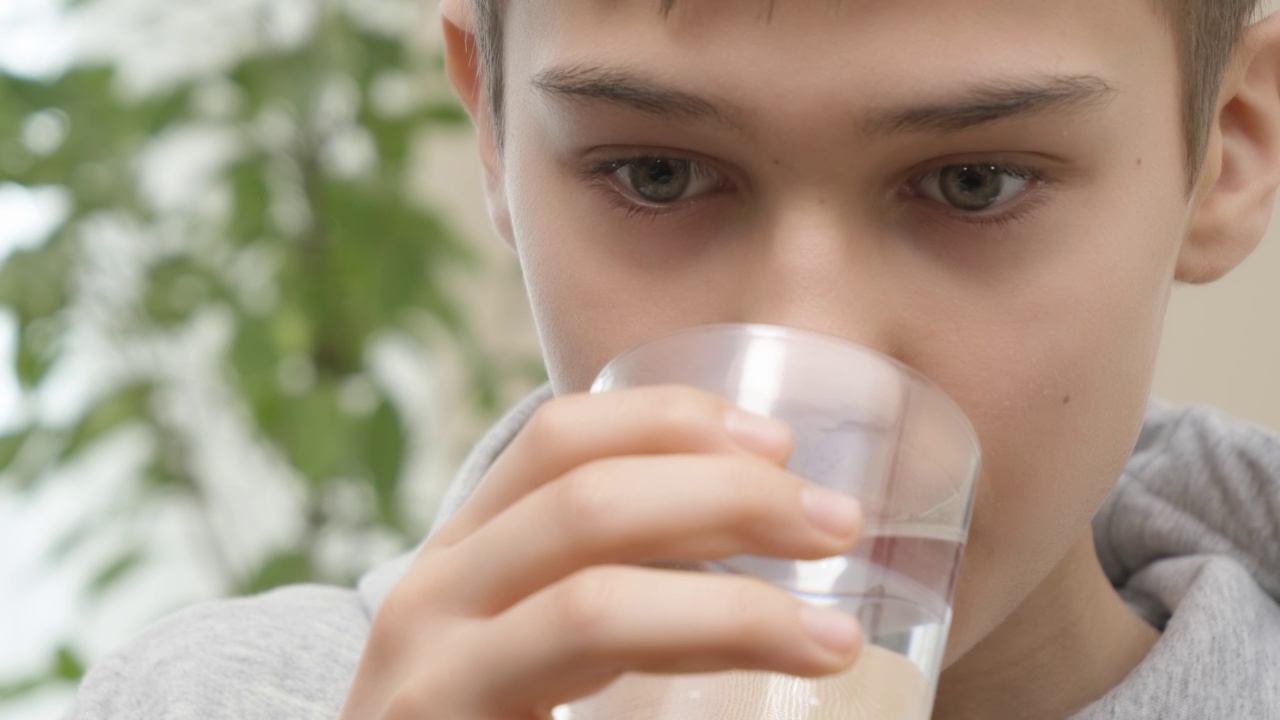 十几岁的男孩服用补品，药物胶囊与一杯水的特写。医疗保健和医学概念。4 k的视频视频下载