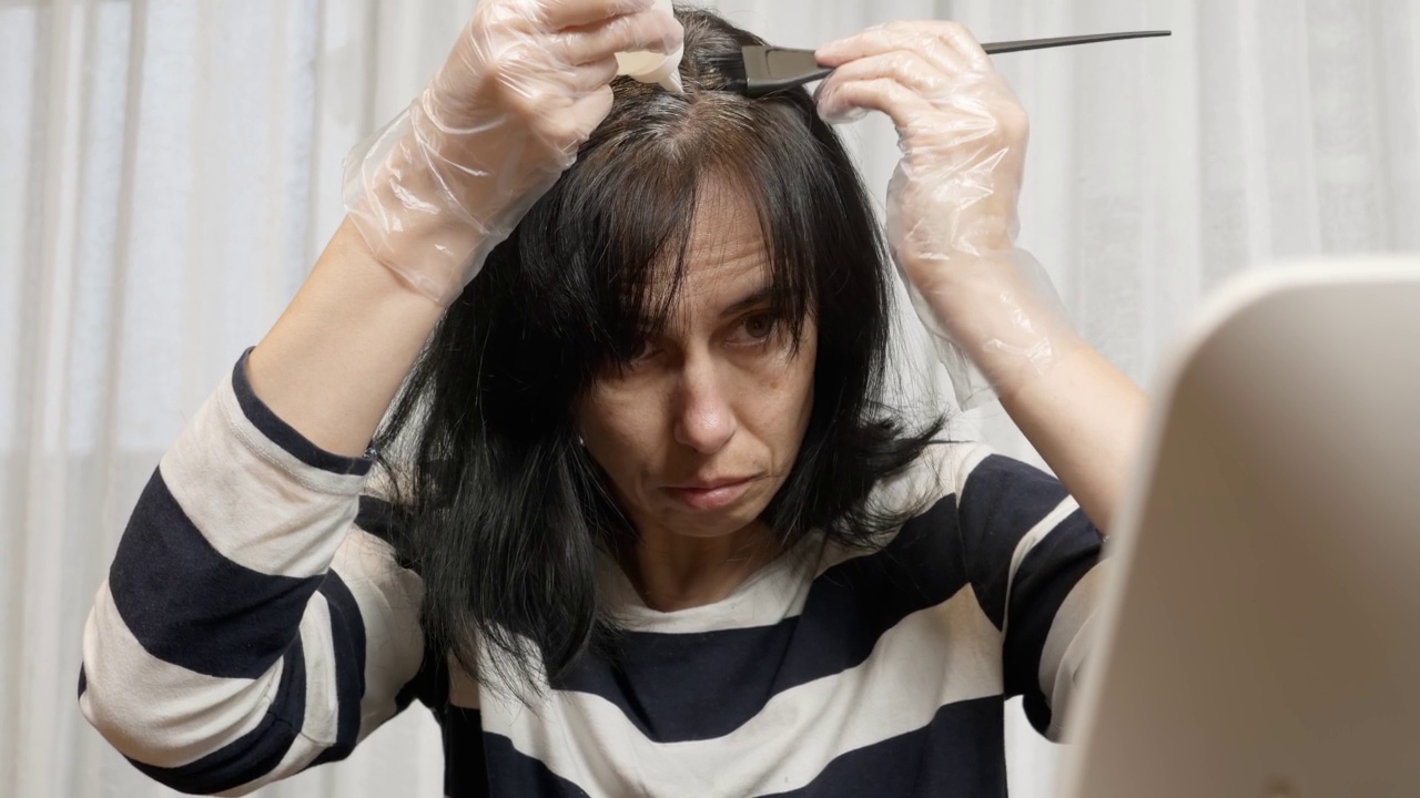 在家染发。一位中年妇女正准备在家染发，看着她乌黑的头发重新长出的灰色根茎视频素材