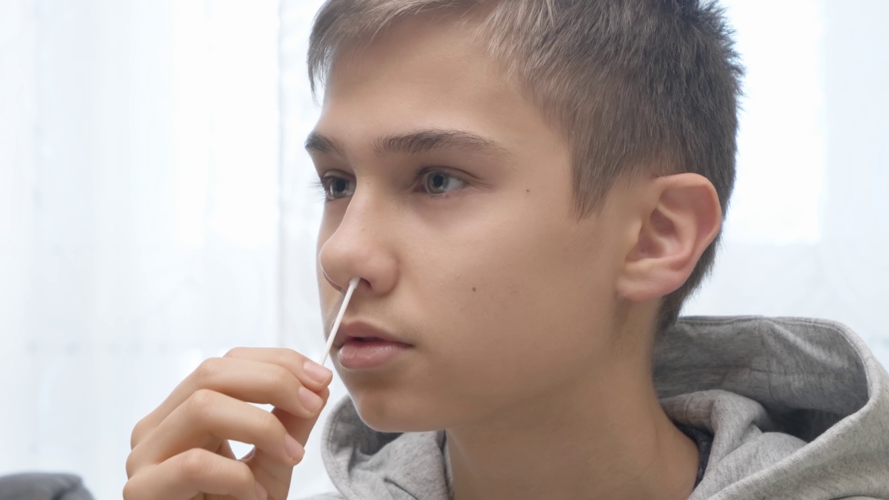 十几岁的男孩正在用快速诊断试剂盒进行Covid-19抗原自检。孩子在上学前在家里用鼻拭子做冠状病毒检测视频下载
