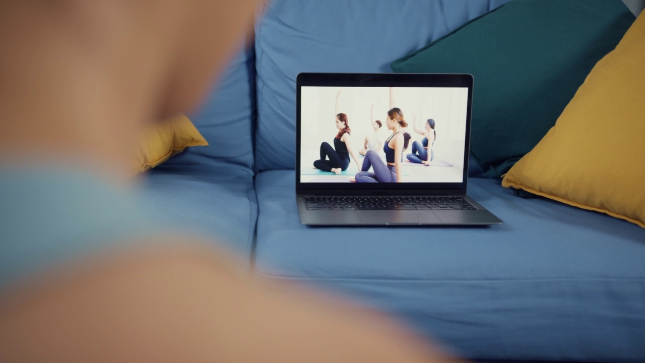 年轻有吸引力的亚洲妇女在运动服装网站垫子在地板上虚拟健身班与一群人在笔记本电脑上的视频会议练习瑜伽初学者在家里的客厅。视频素材