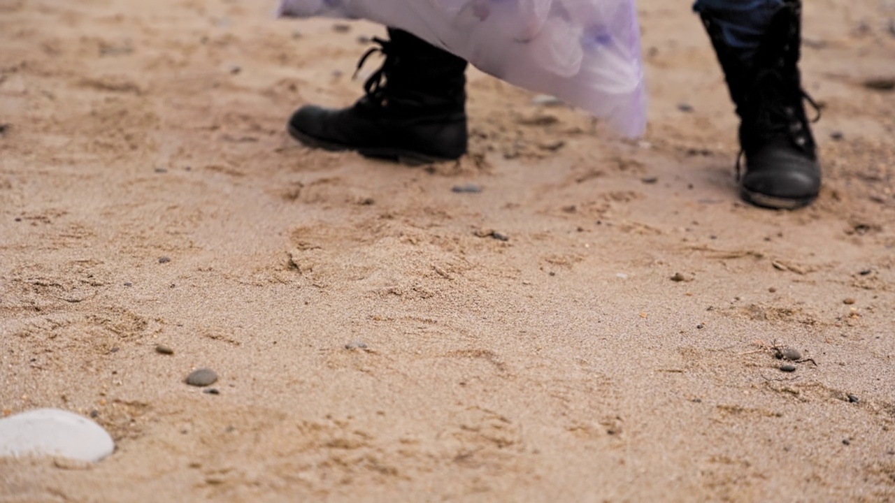 一个人走在沙滩上，用塑料袋收集垃圾。腿特写。低角度。环境保护的概念和地球日视频素材