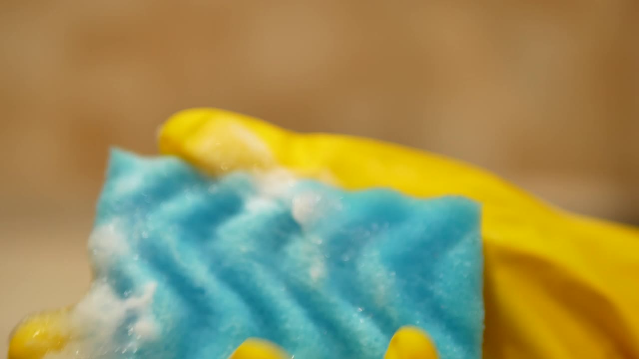 手在黄色清洁手套持有蓝色泡沫海绵，然后开始清洁灶具模糊背景- 4K，特写视频素材