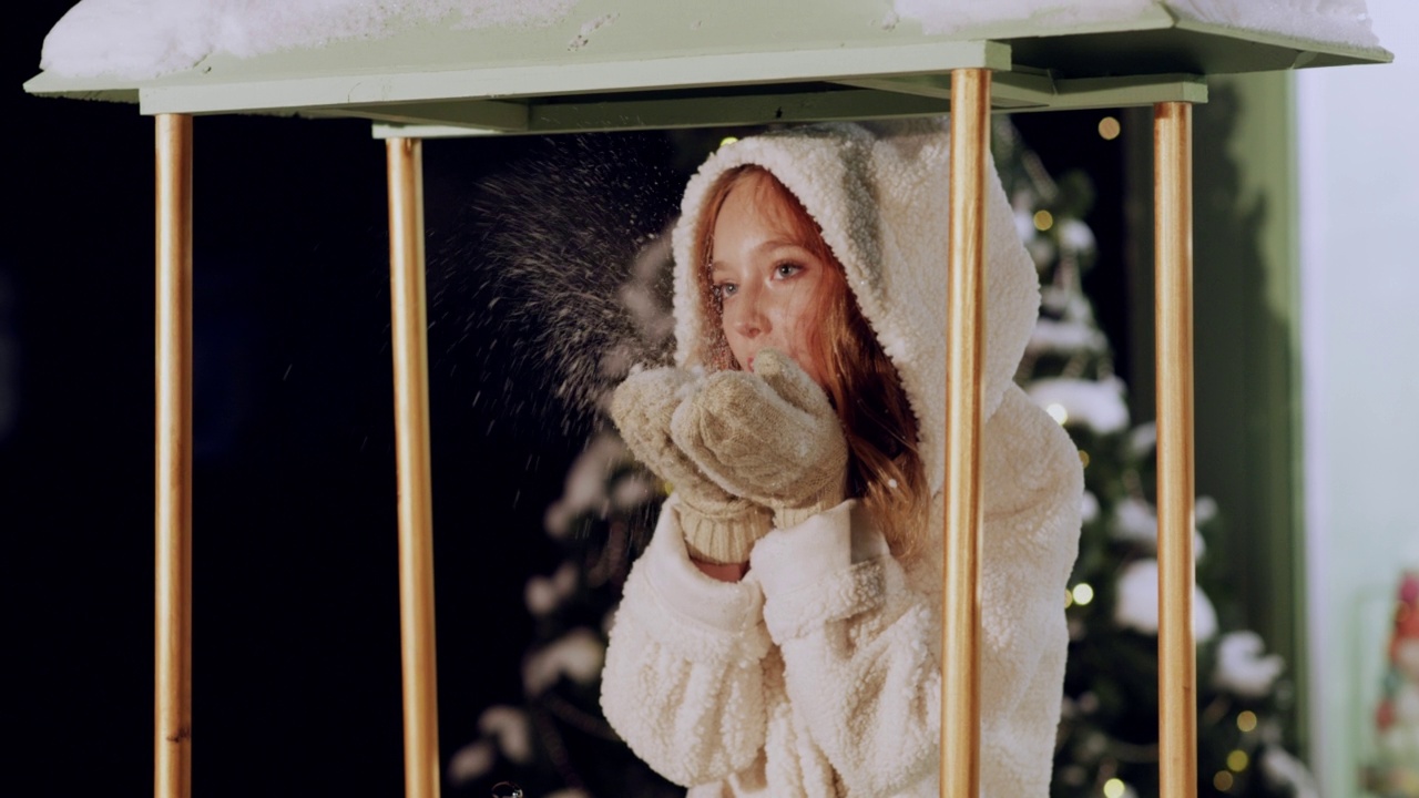 穿着皮草大衣的浪漫少女在冬天从手套里吹雪。冬天，穿着白色外套的美丽女人，从针织手套上吹起雪花。视频素材