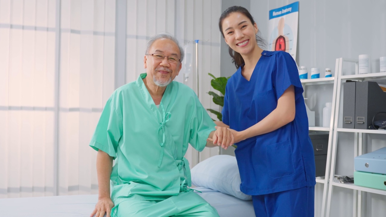 肖像的亚洲女性治疗师和资深男性患者在医院。有吸引力的女性专科医生做物理治疗程序的老年成熟的男性然后看相机在预约期间。视频下载