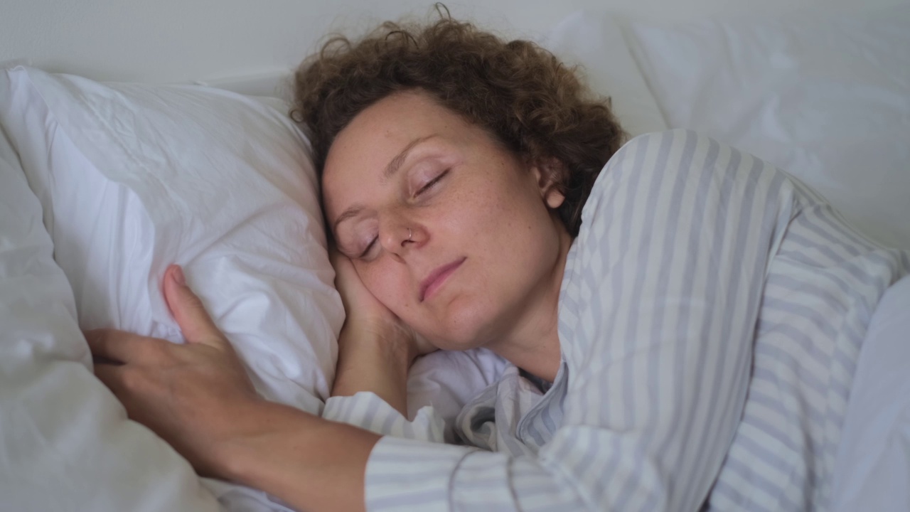 一个穿着轻便睡衣的女人在睡觉。在梦中，身体的运动是任意发生的。一个女人在整理她的枕头。一只手放在头下，方便睡觉视频素材
