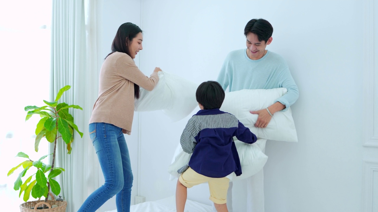 快乐的家庭时间，年轻的亚洲父母正在床上玩枕头与儿子在卧室快乐，笑着微笑。视频素材