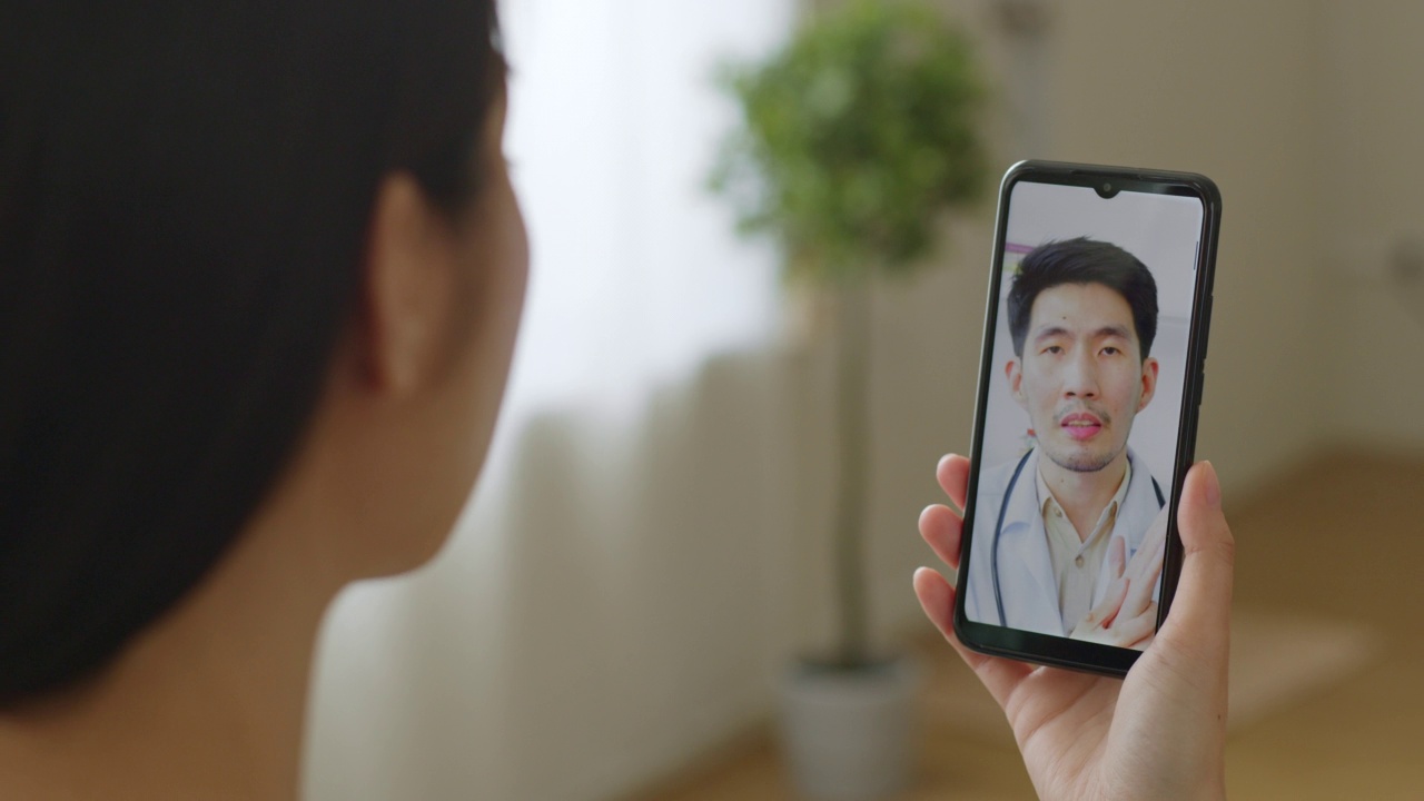 亚洲女性通过移动智能手机虚拟视频电话或在家视频会议与医生交谈，远程保健和远程医疗的概念视频素材