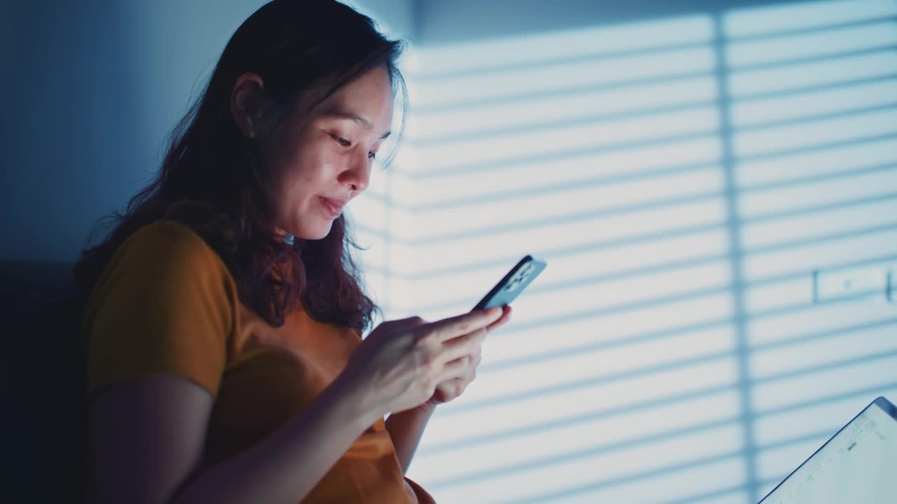 亚洲女性晚上在床上使用智能手机视频素材