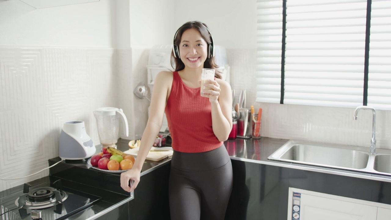 亚洲妇女在运动后做水果奶昔。她正在听音乐视频下载