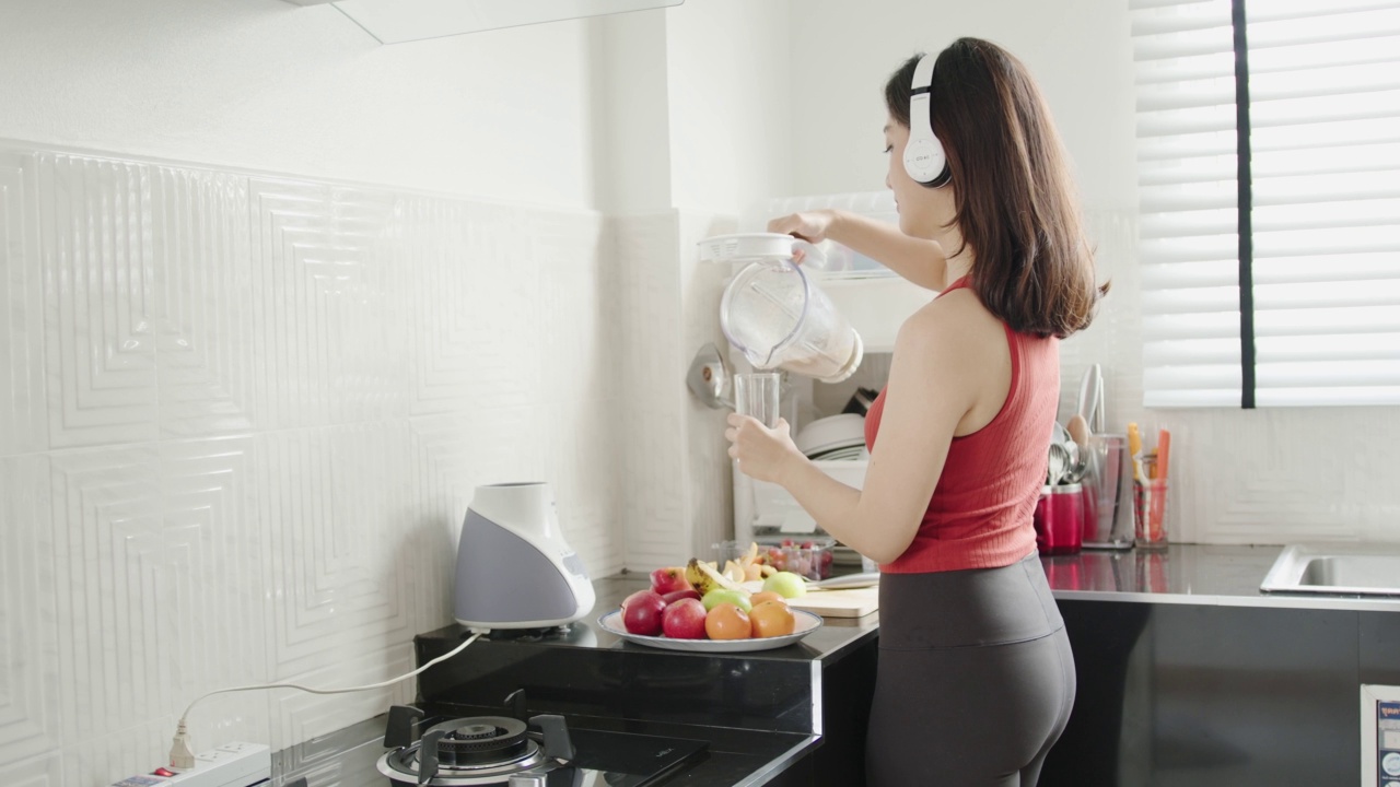 亚洲妇女在运动后做水果奶昔。她正在听音乐视频下载