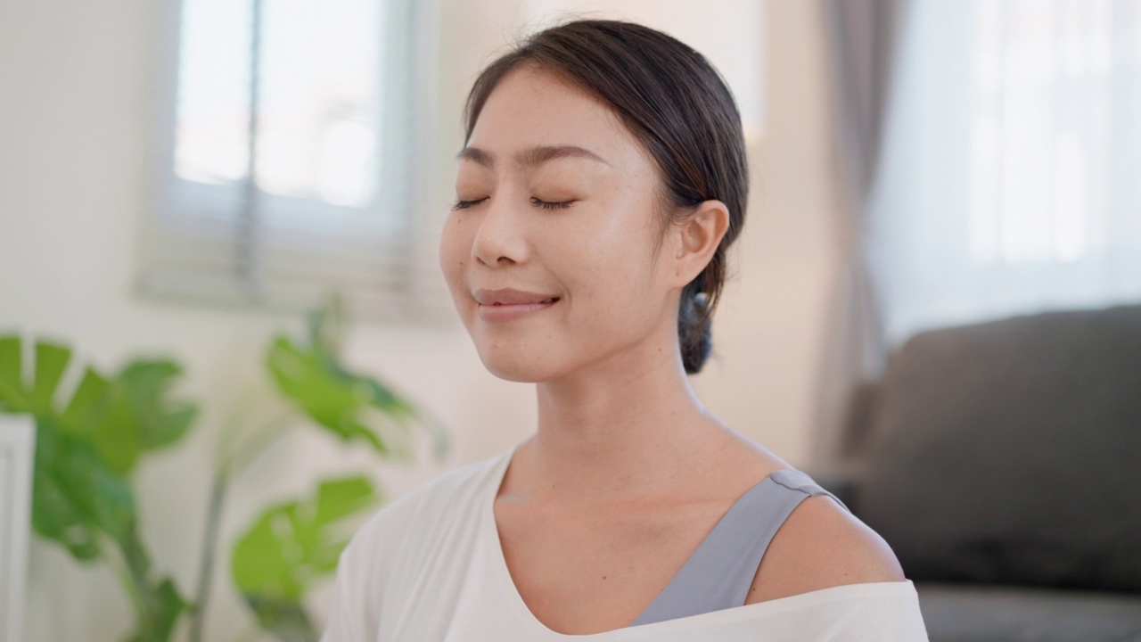 专注于年轻漂亮的亚洲女性练习呼吸专注冥想，舒适地坐着，轻轻地闭上眼睛，慢慢地吸气呼气。缓解压力的呼吸技巧视频素材