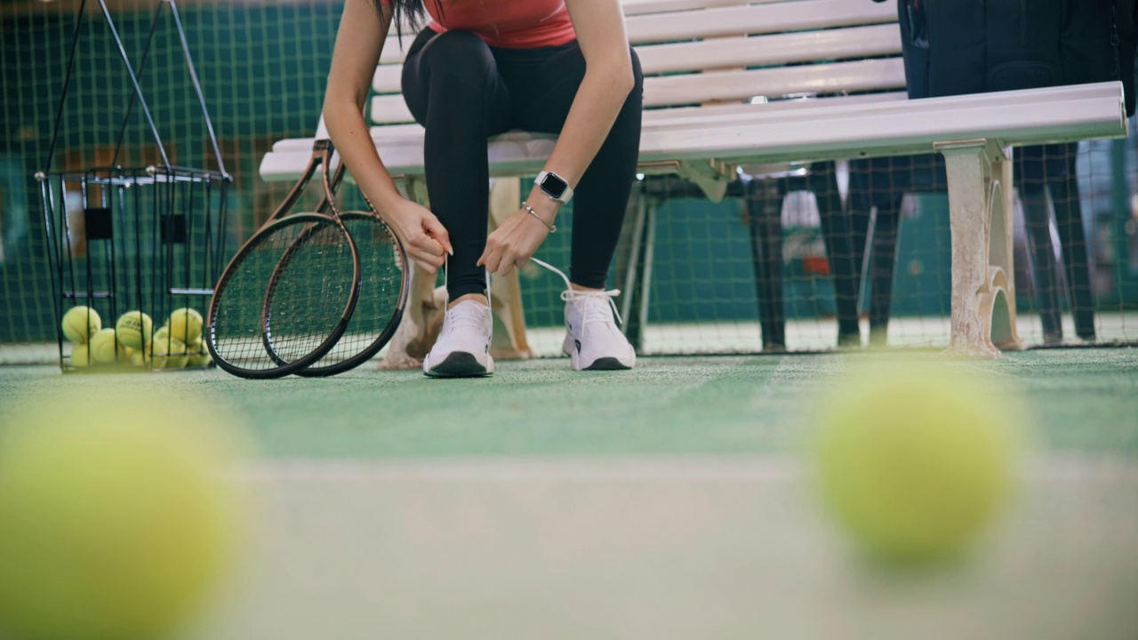 室内网球场，年轻女子坐在长椅上系鞋带视频下载