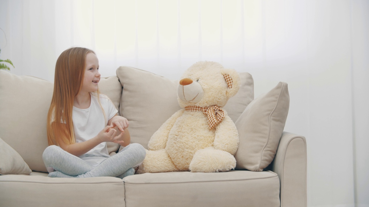 穿着白衣的小女孩与泰迪熊对话的4k慢动作视频。和泰迪熊朋友聊天的概念。视频素材