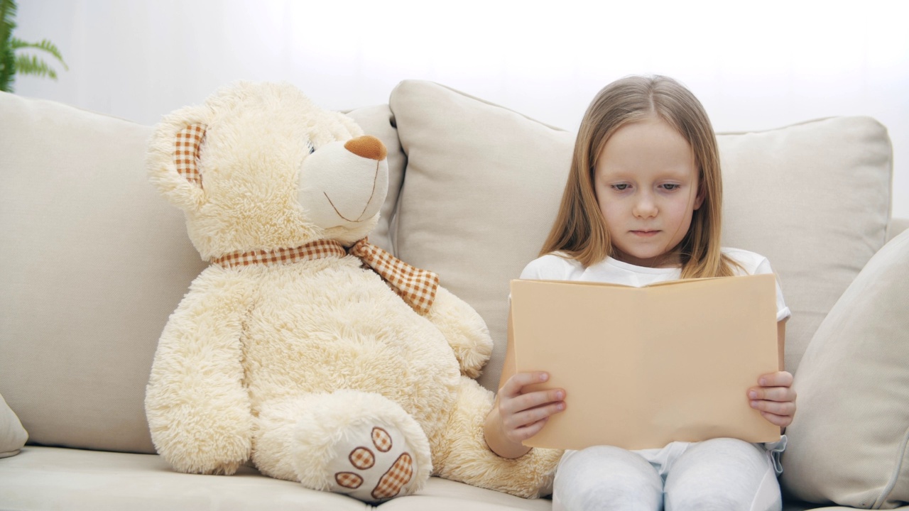 4k视频小女孩和泰迪熊坐在一起，拿着一本书。视频素材