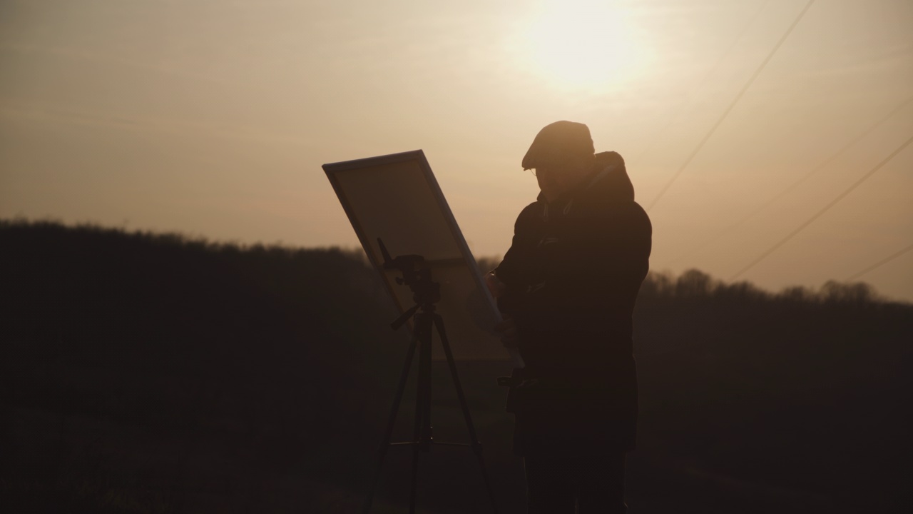 日落时分，一个人在自然上的画架上用颜料在画布上作画视频下载