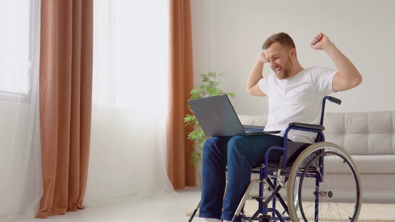 快乐快乐的残疾人坐在轮椅上，带着笔记本电脑庆祝好消息视频下载