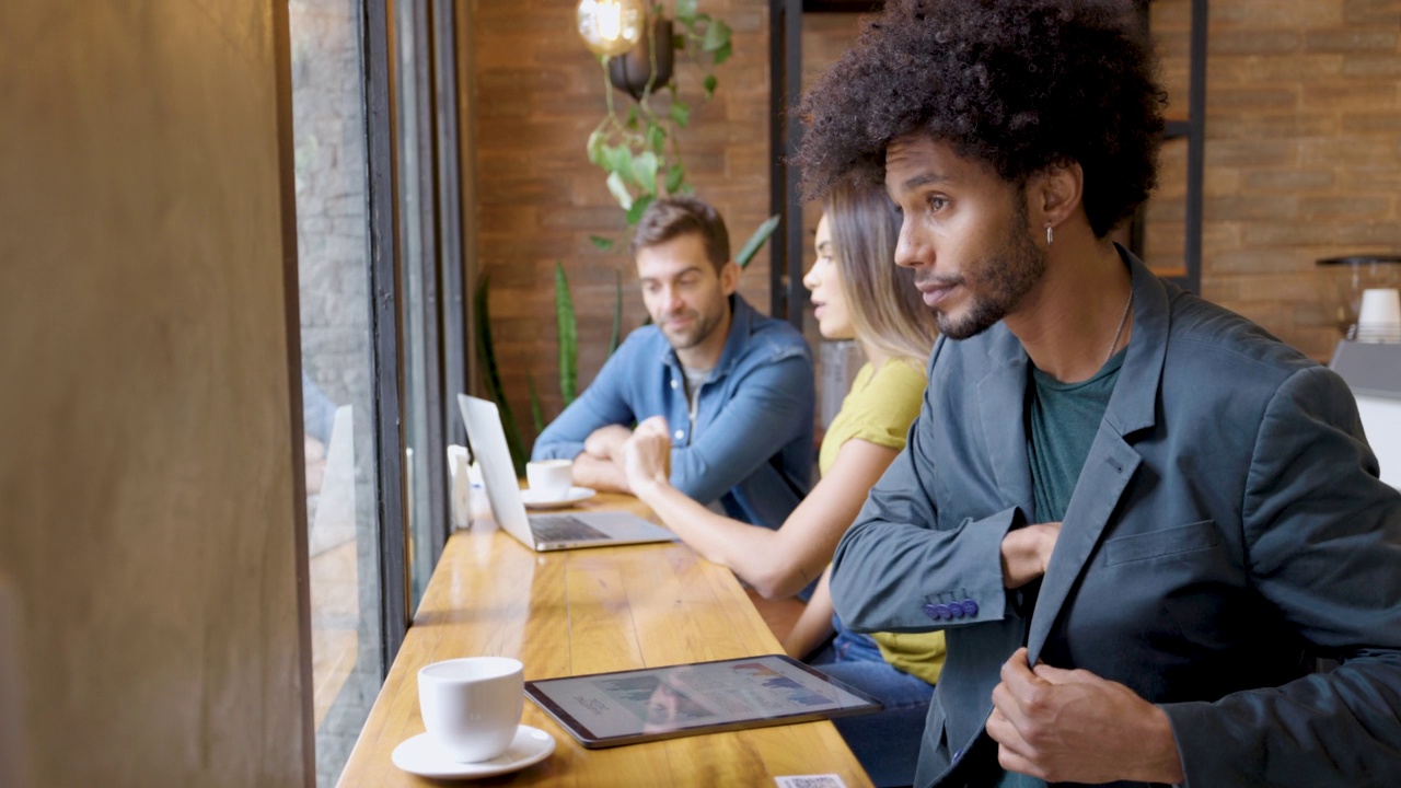 快乐的男性非洲式发型，在咖啡馆边喝咖啡边用平板电脑在线工作视频素材