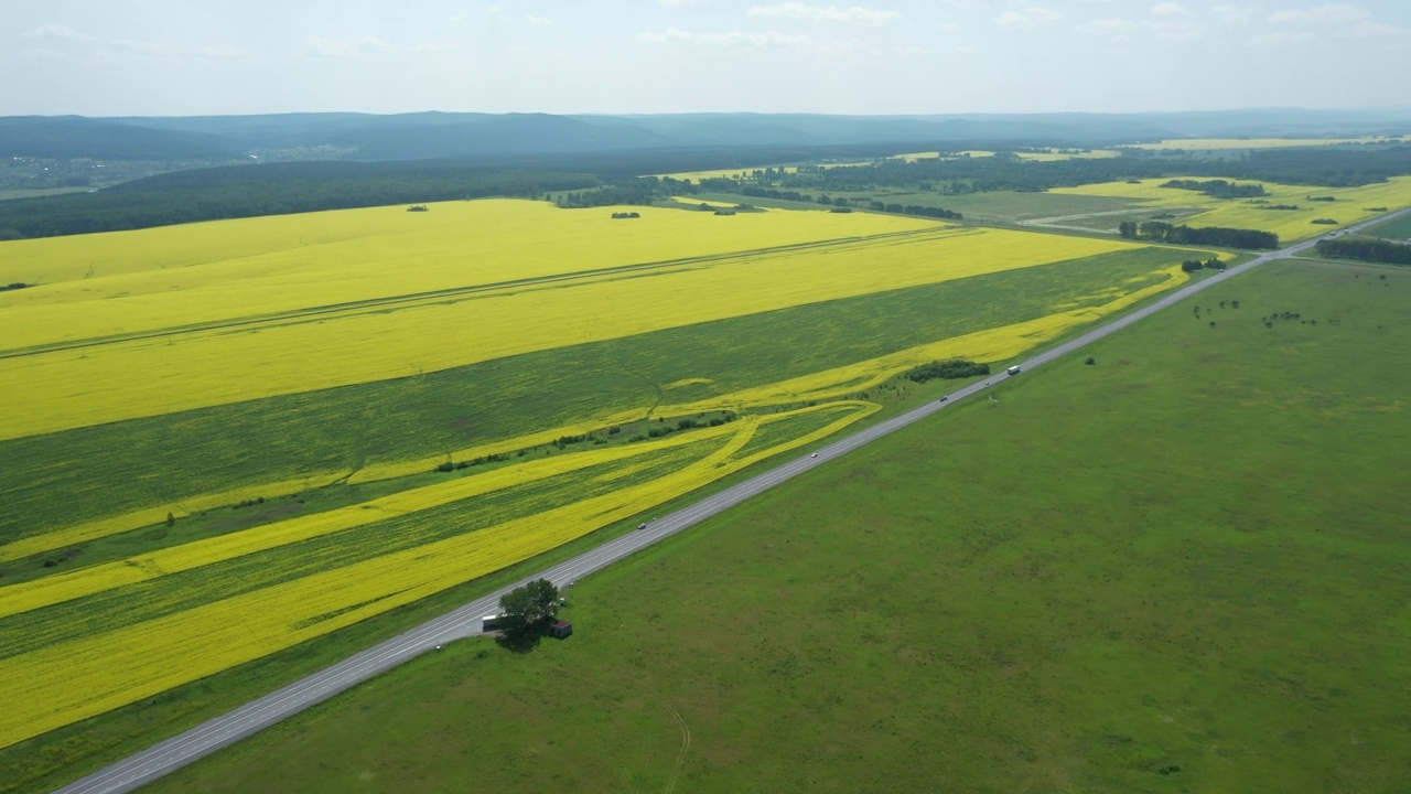 空中飞过沥青城际高速公路通过绿色和黄色的农村田野背景在夏天的早晨。卡车沿路行驶，运送货物和许多汽车视频素材