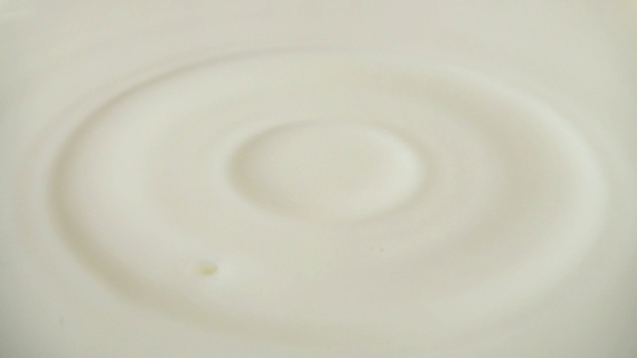 一滴牛奶掉进了乳白色的表面。缓慢的运动。视频素材
