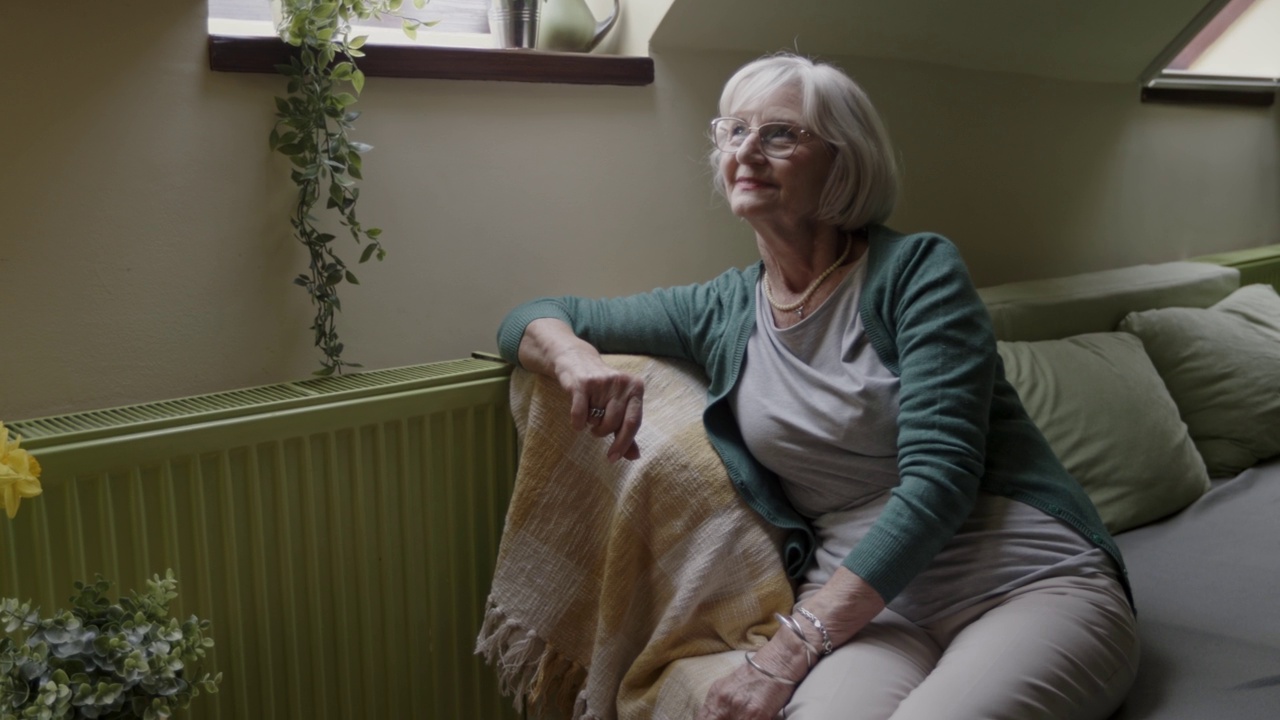 心满意足的老妇人坐在沙发上，微笑着，沉思着视频素材
